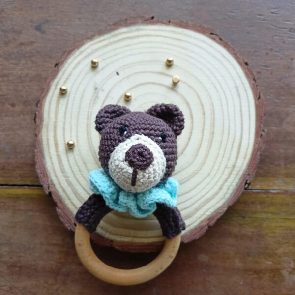 a bear ratlle with blue ruffles on a wooden coaster